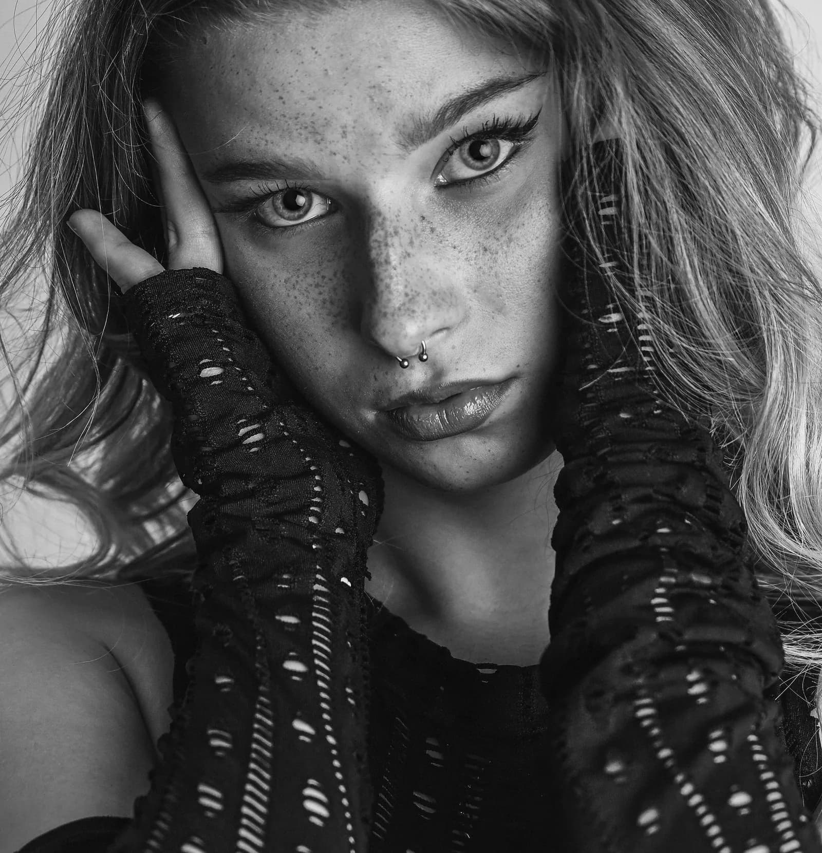 Black and white close-up with freckles, a nose piercing and a mesh glove