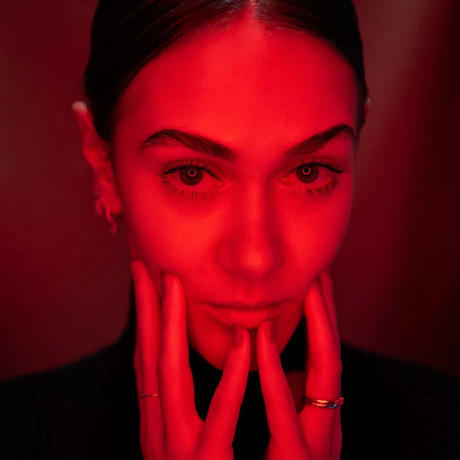 A woman's face in red light, hands beneath her chin